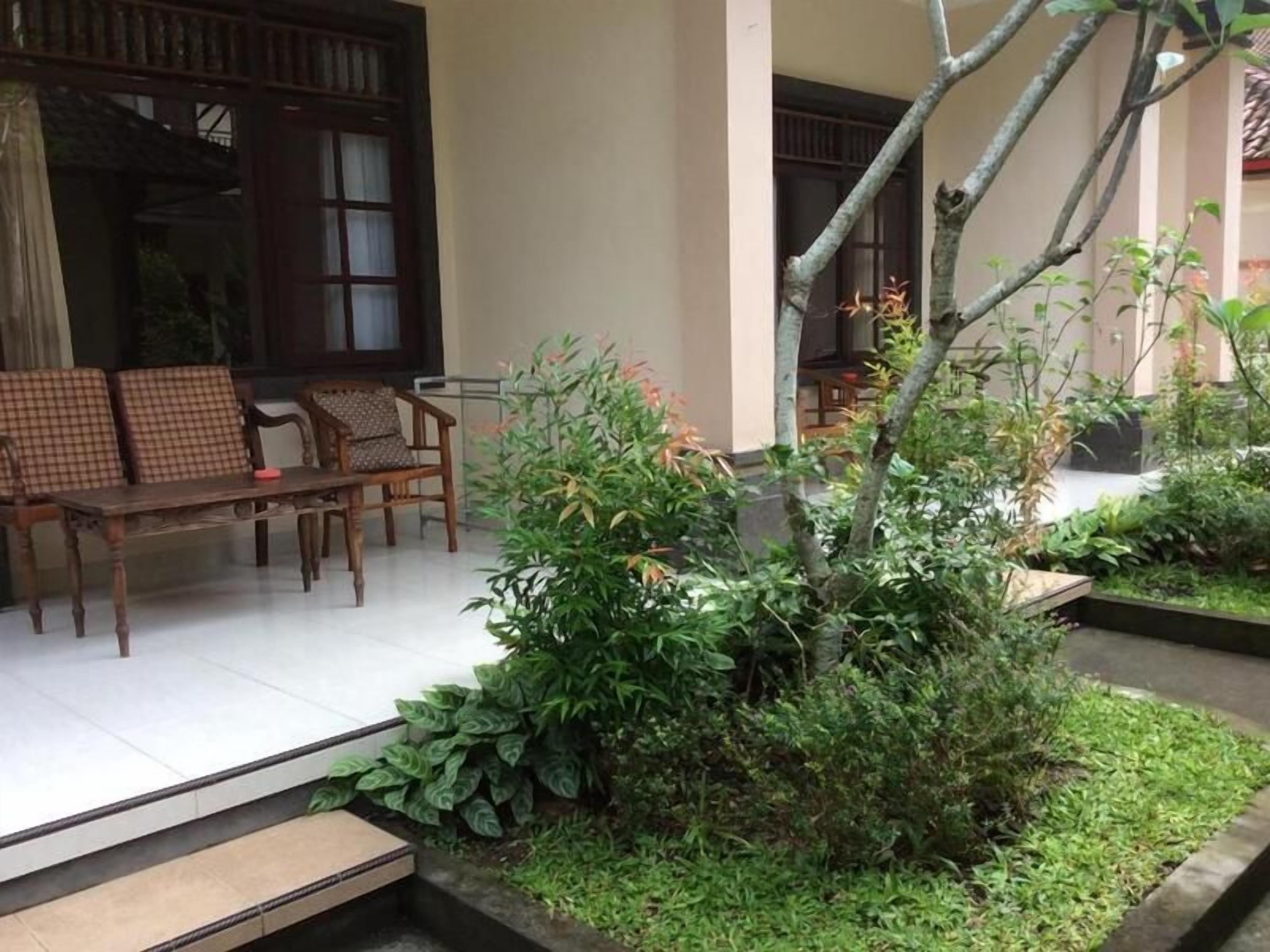 A traditional wooden bench and chairs outside a building with a garden area featuring a small tree and plants.