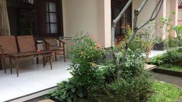 A traditional wooden bench and chairs outside a building with a garden area featuring a small tree and plants.