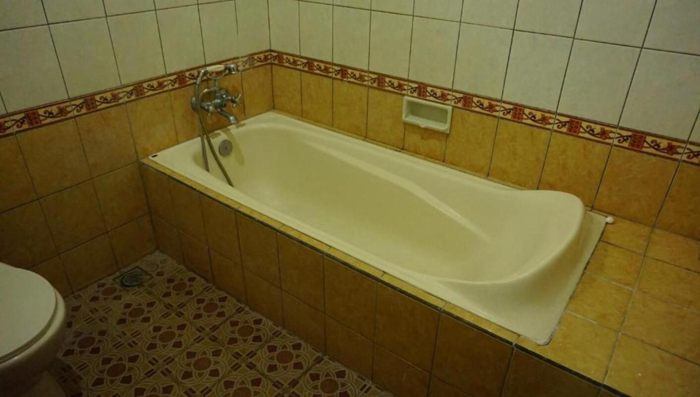A bathroom with a bathtub, toilet, and patterned floor tiles.