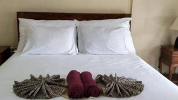 A hotel room with a large bed, two pillows, a colorful abstract painting on the wall, and a neatly arranged towel and patterned cloth on the bed.