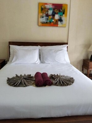 A hotel room with a large bed, two pillows, a colorful abstract painting on the wall, and a neatly arranged towel and patterned cloth on the bed. -  Nyuh Gading Accommodation Ubud (Ubud)