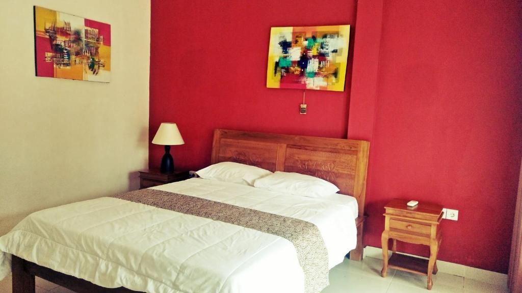 A bedroom with a bed, a nightstand, a lamp, and two abstract paintings on the wall.