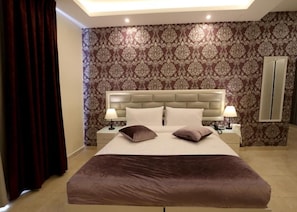 Una habitación de hotel con una cama grande, dos lámparas de noche, un cabecero y un papel tapiz estampado.
