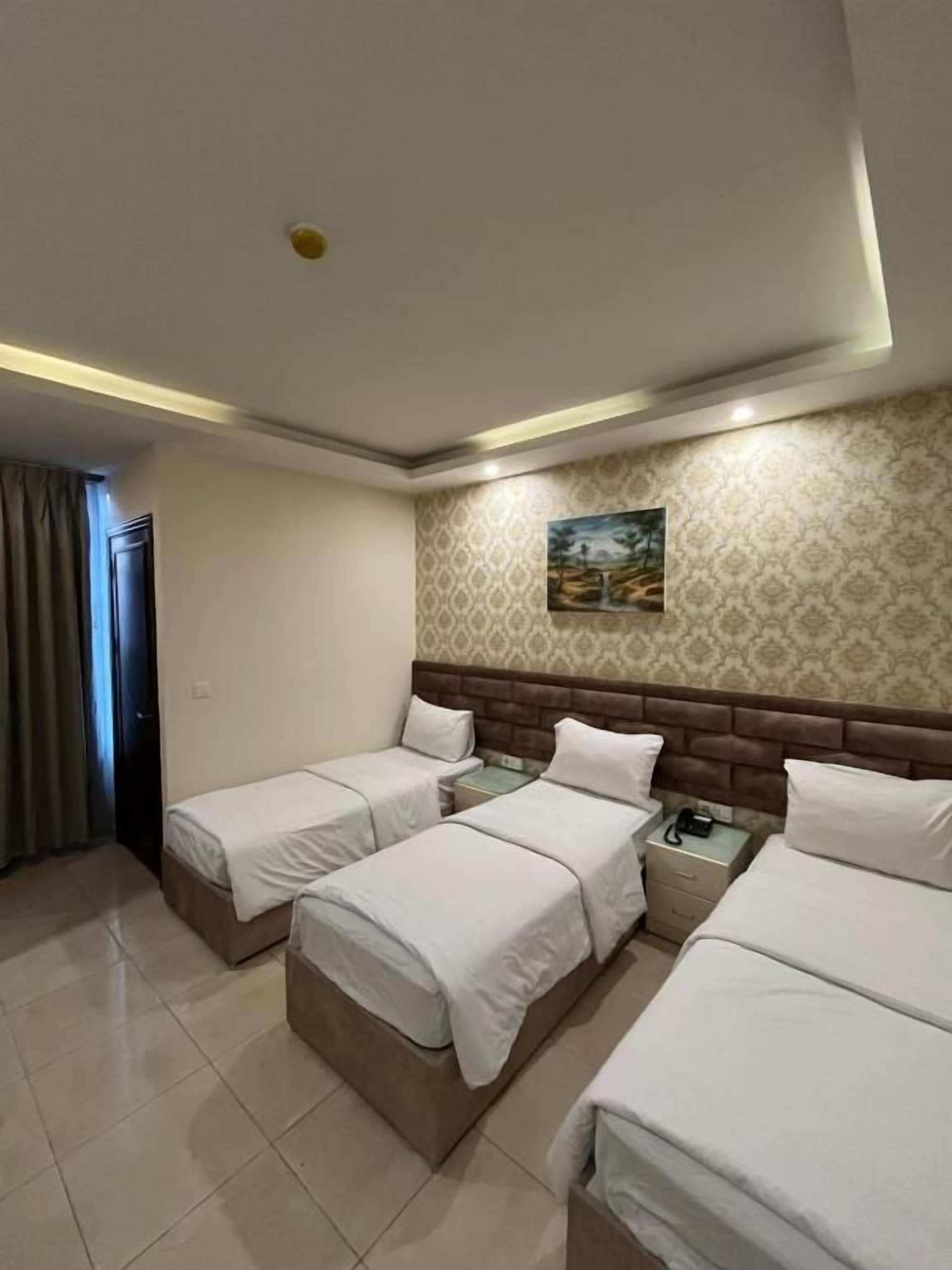 A hotel room with three beds, a nightstand, a wall-mounted painting, and a patterned wallpaper.
