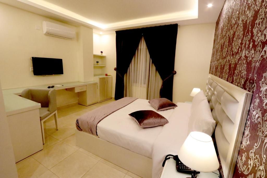 A hotel room with a bed, bedside table, lamp, and a television on the wall.