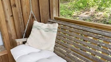 A wooden swing bench with cushions, a chain, and a view of a forested area.
