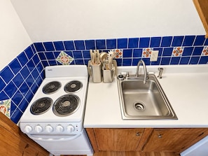 A kitchen with a white stove, a stainless steel sink, and blue-tiled backsplash.