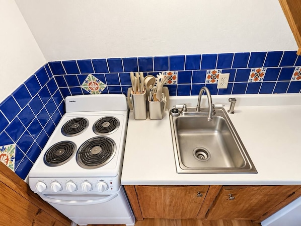 A kitchen with a white stove, a stainless steel sink, and blue-tiled backsplash.