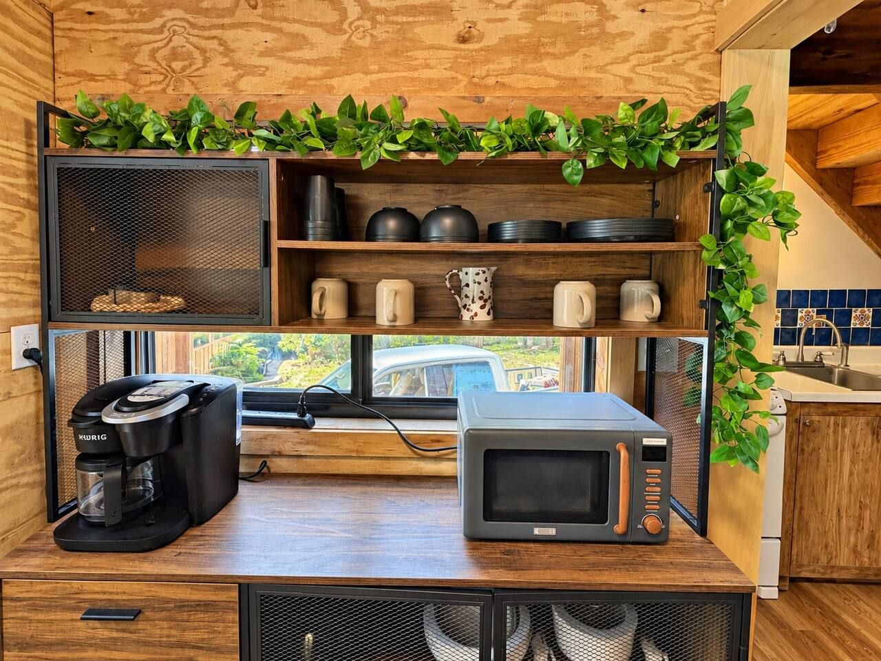 Cocina compacta con cafetera, microondas y estantes con utensilios de cocina.