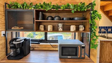 Cocina compacta con cafetera, microondas y estantes con utensilios de cocina.