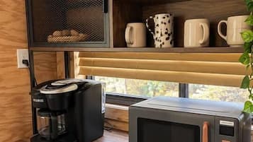 A kitchenette with a coffee maker, microwave, and shelves with mugs and a plant.