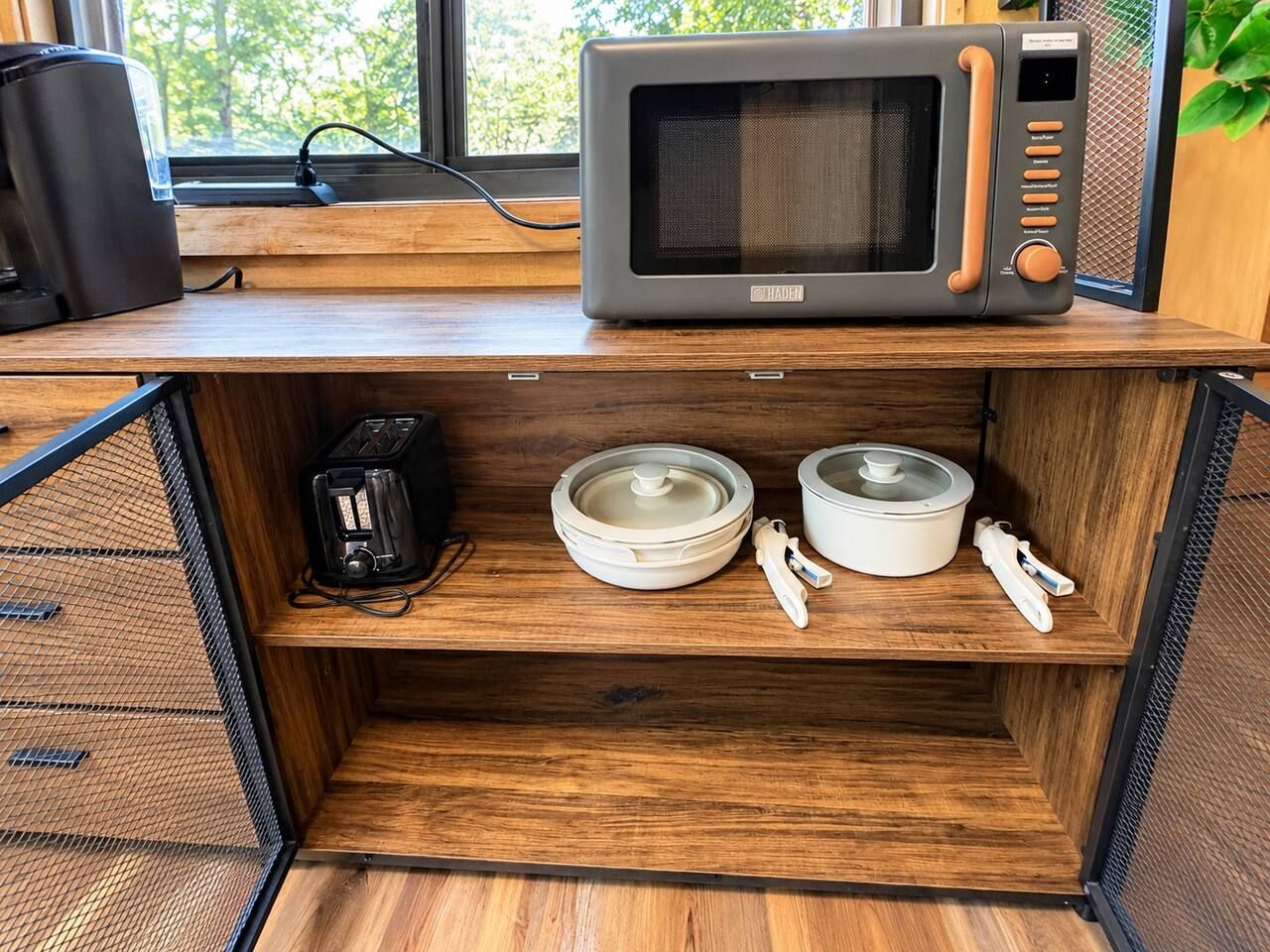 Una zona de cocina con un microondas sobre una encimera de madera, una cafetera y dos recipientes blancos con tapas.