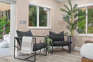 A modern room with a large window, two black chairs with cushions, a white bed, and a potted plant. - Ft Lauderdale Villa Heated Pool + Arcades, Huge TV + yard (Fort Lauderdale)