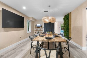 A modern dining area with a wooden table, black chairs, and a large woven light fixture. - Ft Lauderdale Villa Heated Pool + Arcades, Huge TV + yard (Fort Lauderdale)