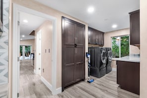 A modern kitchen with dark cabinets, a built-in washer and dryer, and a view of the outdoors. - Ft Lauderdale Villa Heated Pool + Arcades, Huge TV + yard (Fort Lauderdale)