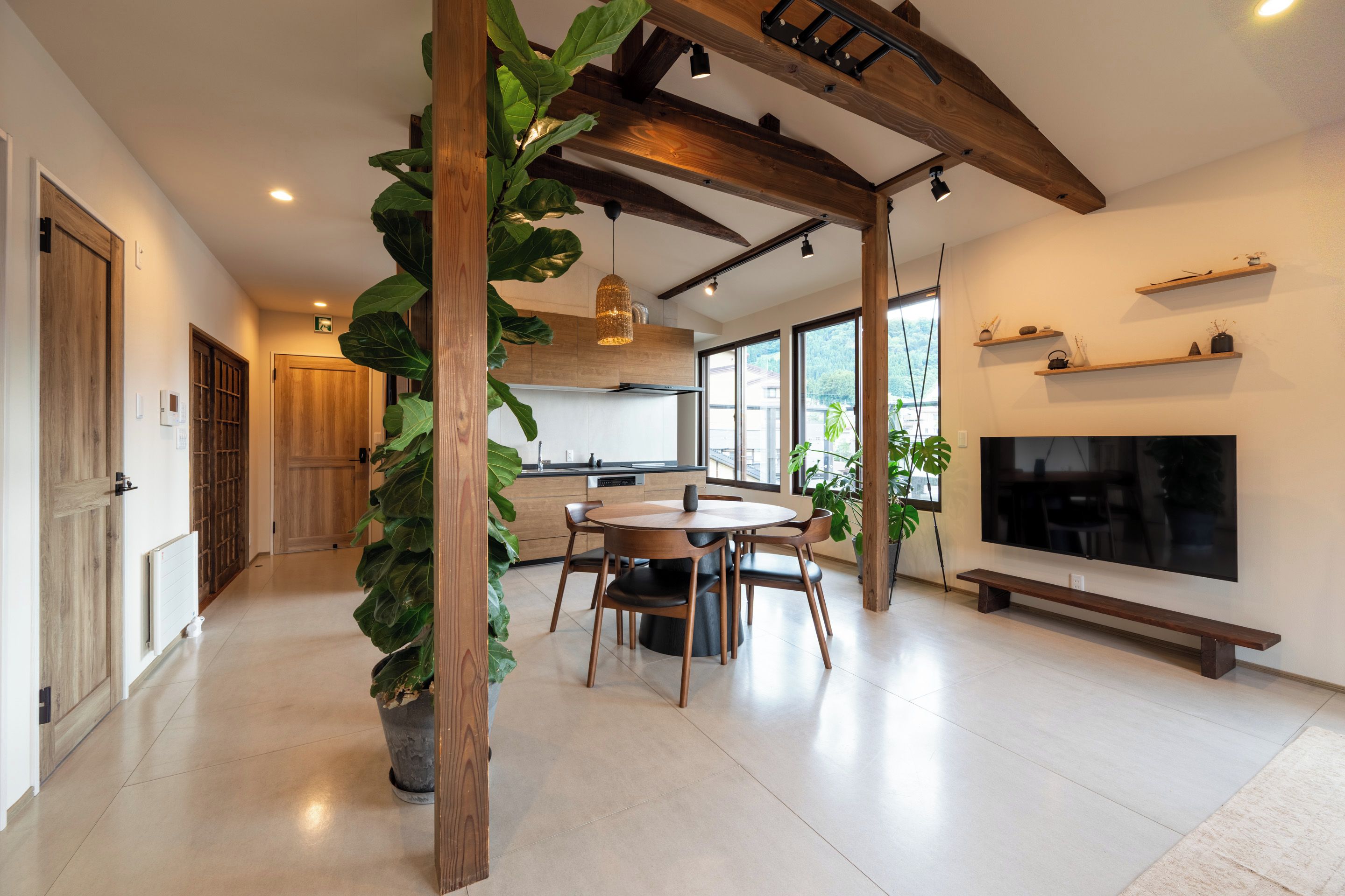 A modern kitchen with wooden beams, a dining area with a round table, and a large window providing a view of the outdoors.