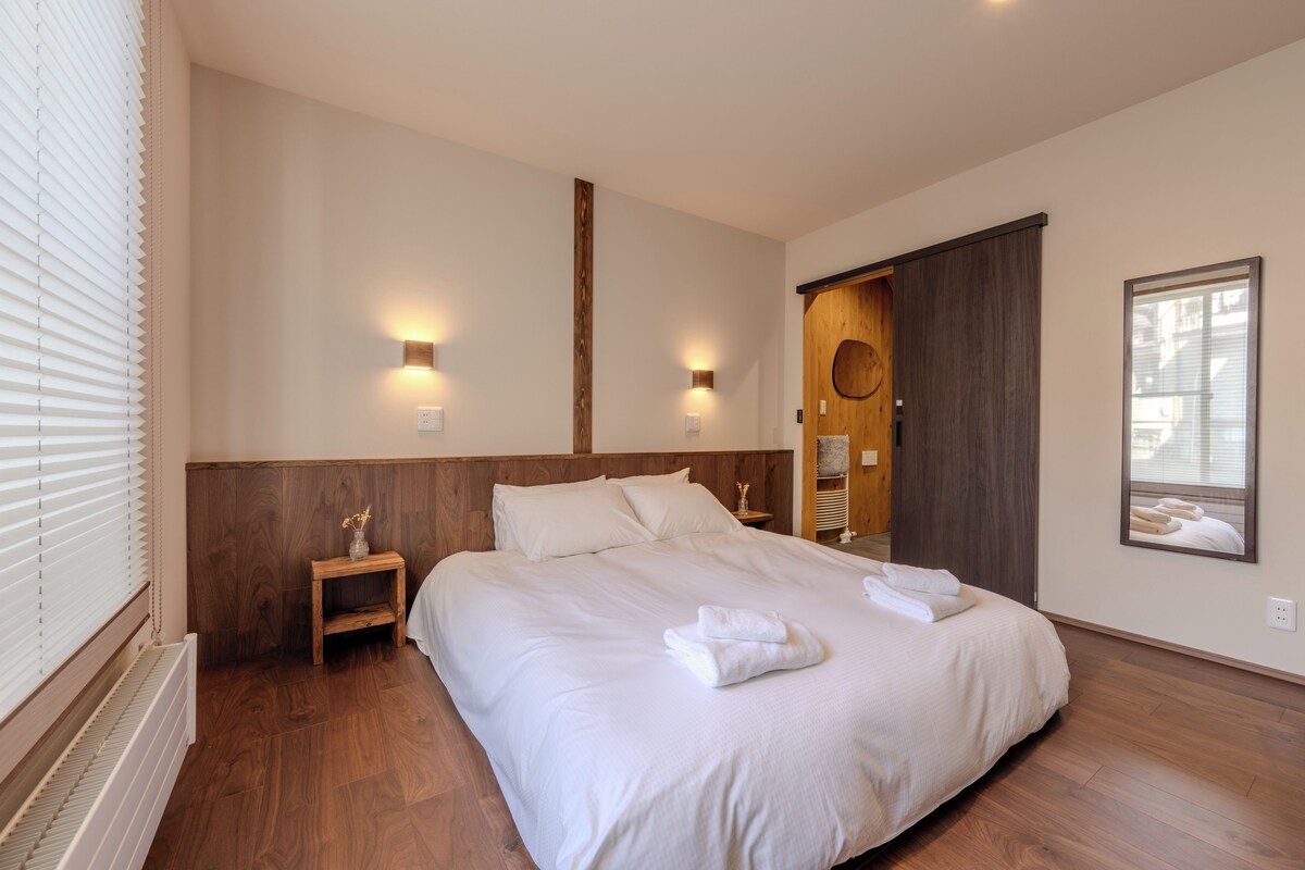 A bedroom with a large bed, wooden headboard, bedside lamps, a nightstand, and a mirror.