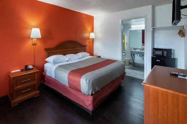 A hotel room with a bed, bedside tables, a desk, a microwave, and a bathroom visible through an open door.