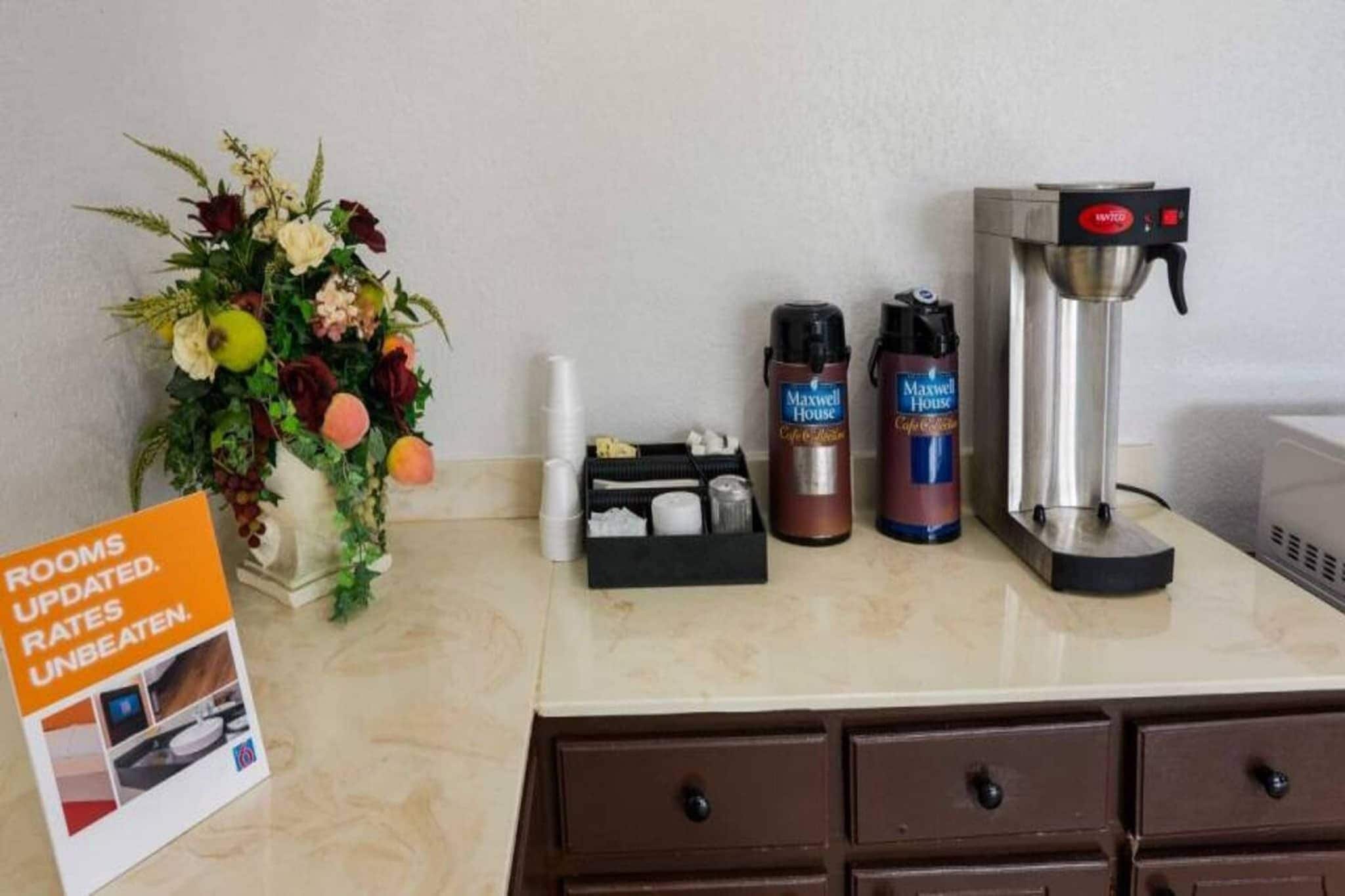 A hotel room counter with a coffee maker, thermos flasks, a tissue box, and a sign about updated room rates.