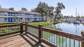 A wooden deck overlooking a marina with boats, a building with blue doors, and trees in the background.