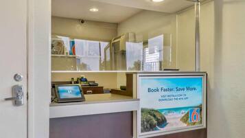 A reception desk with a computer, a phone, and a digital display. There is a poster advertising a mobile app.