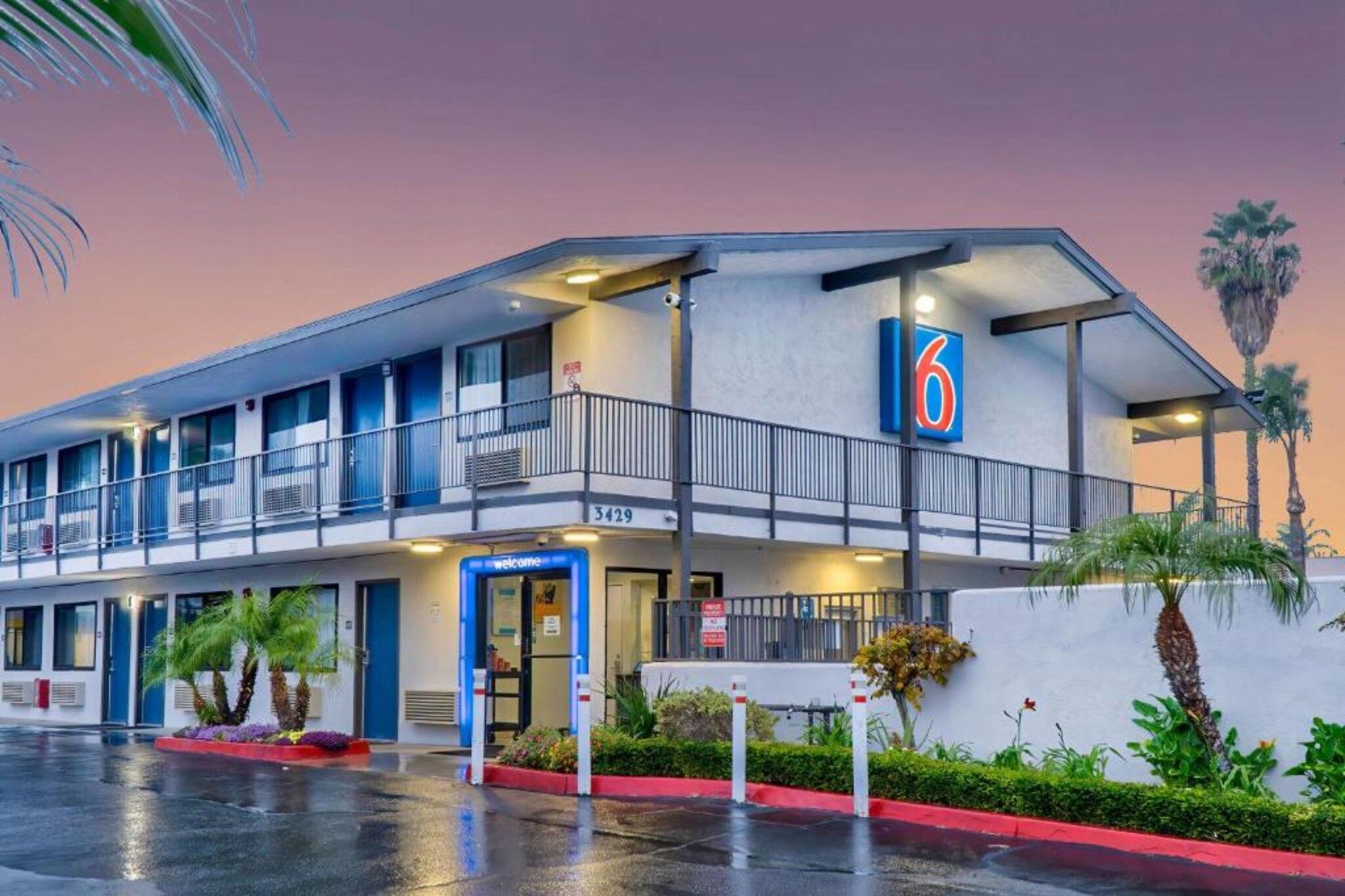 A motel with a blue and white exterior, a balcony on the second floor, and a '6' sign indicating the building number.