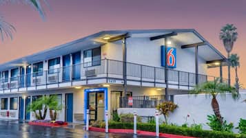 A motel with a blue and white exterior, a balcony on the second floor, and a '6' sign indicating the building number.