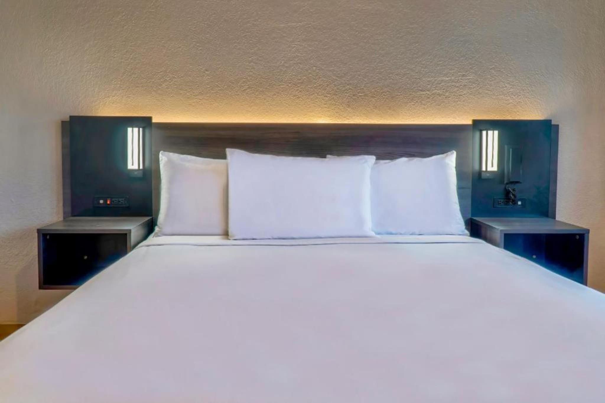 A hotel room with a large bed, two bedside tables, and wall-mounted lighting.