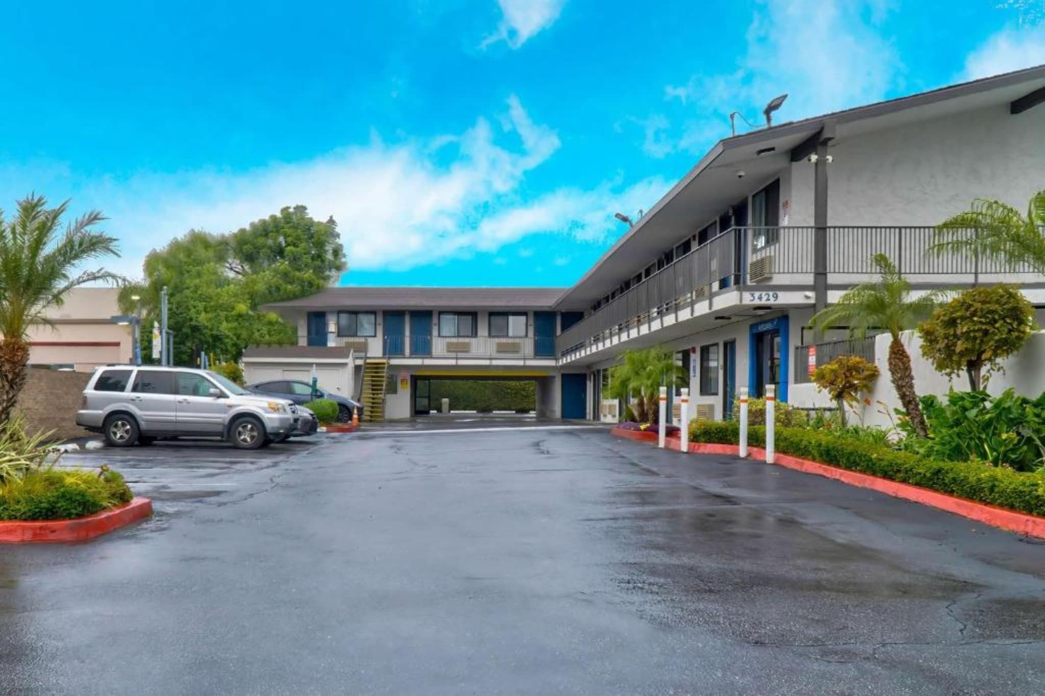 A two-story motel with a covered parking area, a visible entrance, and a clear sky.
