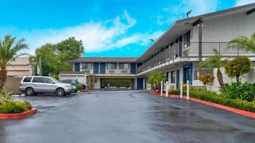 A two-story motel with a covered parking area, a visible entrance, and a clear sky.