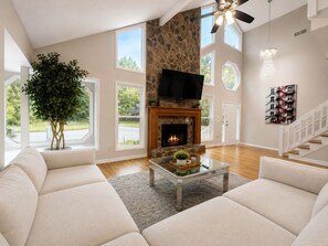A spacious living room with a stone fireplace, a large television, and a staircase. - Spacious 4BR Lawrenceville Home (Lawrenceville)