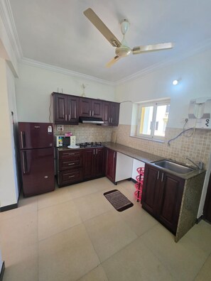 A kitchen with dark wood cabinets, a built-in stove, a refrigerator, and a ceiling fan. - Charming 2-bedroom apartment with AC , POOL & GYM in gorgeous Goa (Goa)