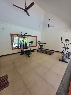 A gym with exercise equipment, a ceiling fan, and a large mirror. - Charming 2-bedroom apartment with AC , POOL & GYM in gorgeous Goa (Goa)