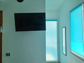 Ein Zimmer mit großem Fenster, einer Tür und einem Lichtschalter an der Wand.
