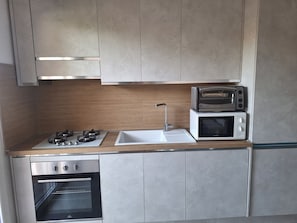 A compact kitchen with a built-in oven, a microwave, and a gas stove. - Cottage in Villasimius (Villasimius)