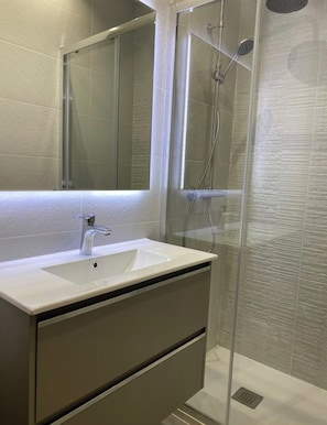 Un bany modern amb dutxa de vidre, un lavabo amb mirall i un moble de banys amb calaixos.