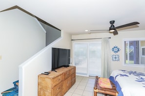 A bedroom with a bed, a television on a wooden cabinet, a ceiling fan, and a window with blinds. - Walk to Shore! Waimanalo Beach Cottages, Unit 9 (Waimanalo)