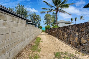 A pathway flanked by a stone wall and a concrete wall, leading to a building with a sloped roof. - Walk to Shore! Waimanalo Beach Cottages, Unit 9 (Waimanalo)