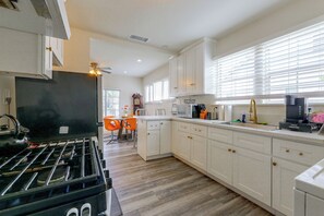 Une cuisine moderne avec des meubles blancs, une cuisinière à gaz, un four à micro-ondes et une machine à café.