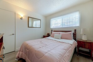 Ein Schlafzimmer mit Bett, Nachttisch, Kommode, Spiegel und Fenster mit Jalousien.