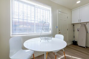Ein kleiner, heller Raum mit einem runden Tisch, zwei Stühlen, einem Fenster mit Jalousien, einer Tür und einem Schrank.