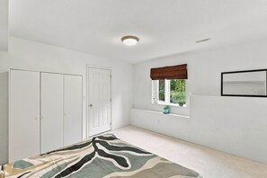 A bedroom with a bed, a wardrobe, a window with a view of greenery, and a ceiling light.