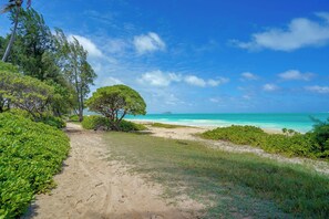 Trilho costeiro que leva a uma praia com águas turquesa cristalinas e céu limpo.