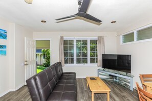 A living room with a sofa, a television, a coffee table, and a ceiling fan. - Walk to Ocean! Waimanalo Beach Cottages: Unit 5 (Waimanalo)