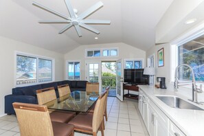 A modern kitchen with a dining area, large windows, and a ceiling fan. - Extended Escape! Waimanalo Beach Cottages, Unit 11 (Waimanalo)