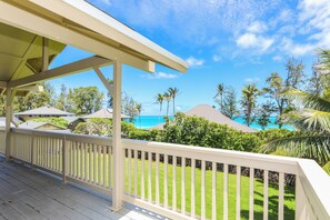A wooden deck with a white railing, overlooking a tropical landscape with palm trees and a view of the ocean. - Extended Escape! Waimanalo Beach Cottages, Unit 11 (Waimanalo)