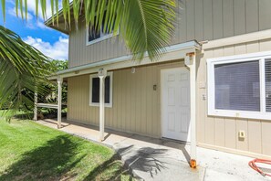 A two-story house with a covered porch, a garage door, and a large window with blinds. - Steps to Beach! Waimanalo Beach Cottages, Unit 10 (Waimanalo)