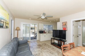 A living room with a sofa, a television, and a dining area with a table and chairs. - Steps to Beach! Waimanalo Beach Cottages, Unit 10 (Waimanalo)