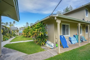 A residential property with a covered porch, a well-maintained lawn, and a collection of surfboards and boogie boards. - Waimanalo Beach Cottages - Large Studio, Unit 4 (Waimanalo)