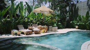 A poolside area with lounge chairs, a thatched umbrella, and tropical plants. - Khubani Resort (Ashvem)